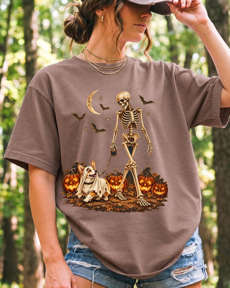 A skeleton walking a corgi in a ghost costume past carved pumpkins under a crescent moon