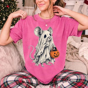Etched pen illustration of a small mouse in a sheet ghost costume holding a candy bucket, bone white with orange accent