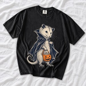 Etched pen illustration of an opossum in a vampire cape holding a candy pumpkin, bone white with orange accent