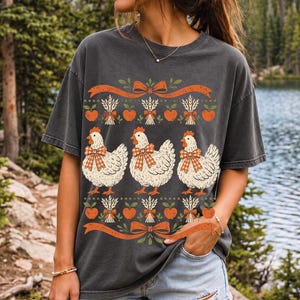 Three fluffy hens with gingham bows between apple and wheat borders, retro folk art fall t-shirt design