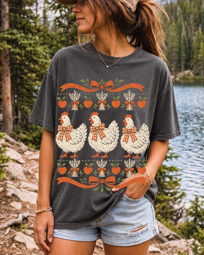 Three fluffy hens with gingham bows between apple and wheat borders, retro folk art fall t-shirt design