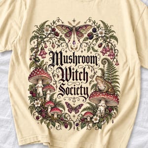 Blackletter text "Mushroom Witch Society" framed by fly agaric mushrooms, ferns and a toad on a mushroom cap