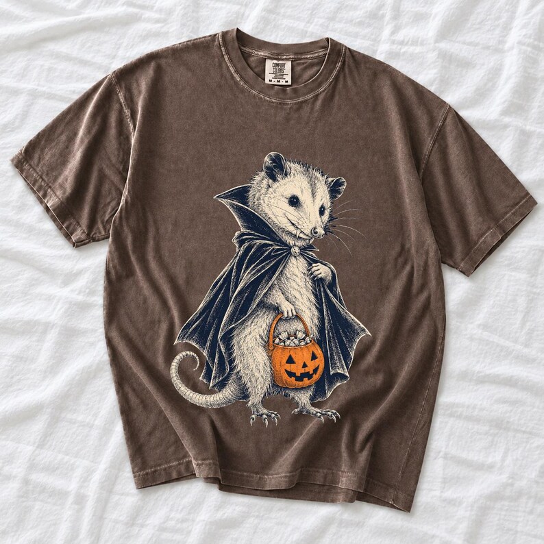 Etched pen illustration of an opossum in a vampire cape holding a candy pumpkin, bone white with orange accent