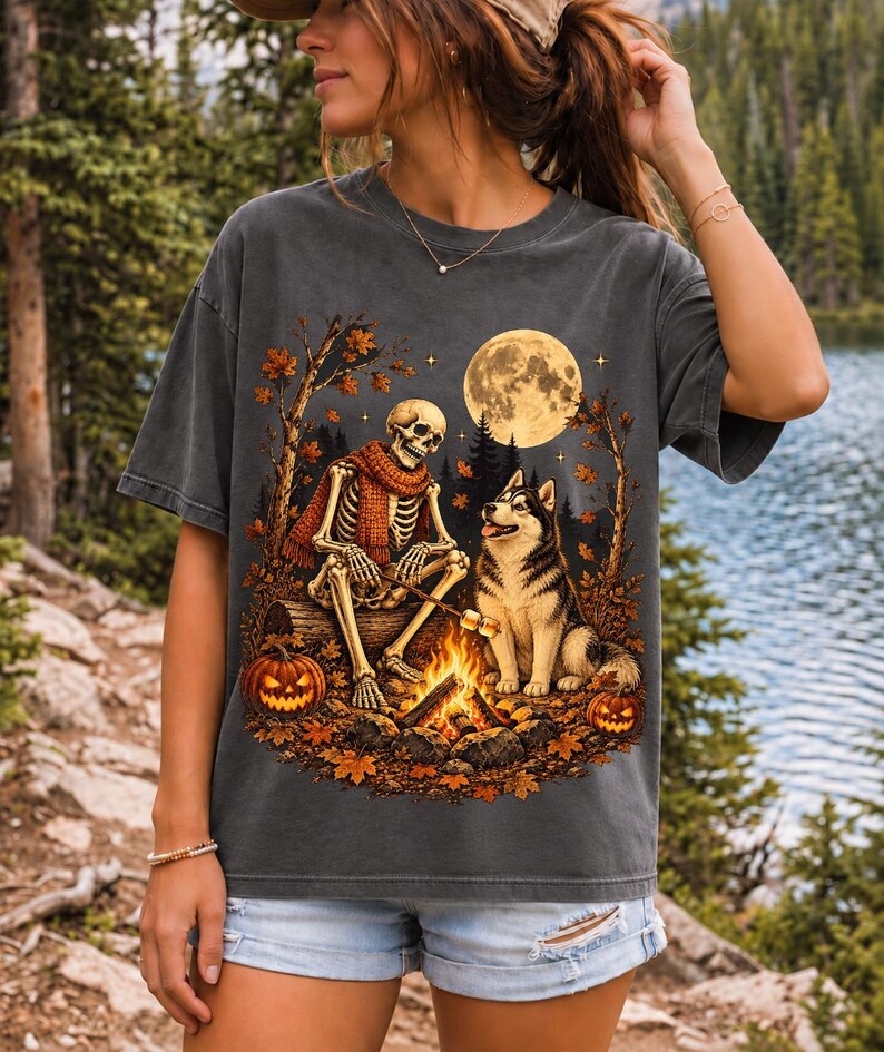 A skeleton in a scarf roasting marshmallows by a campfire beside a husky in an autumn forest under a full moon
