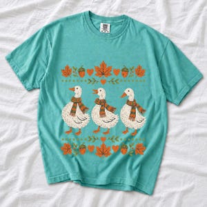 Three white ducks in striped scarves with acorn and maple leaf borders, retro screen print fall t-shirt art