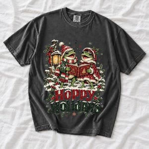 Two frogs singing carols in the snow with a lantern and songbook, text Hoppy Holidays