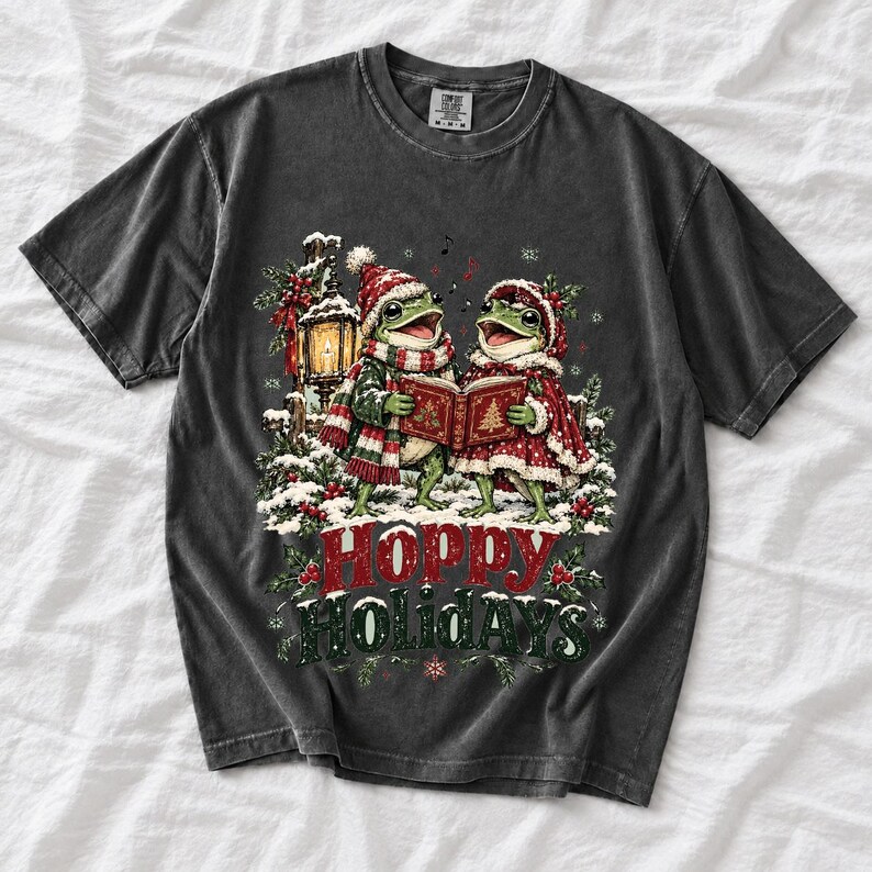 Two frogs singing carols in the snow with a lantern and songbook, text Hoppy Holidays