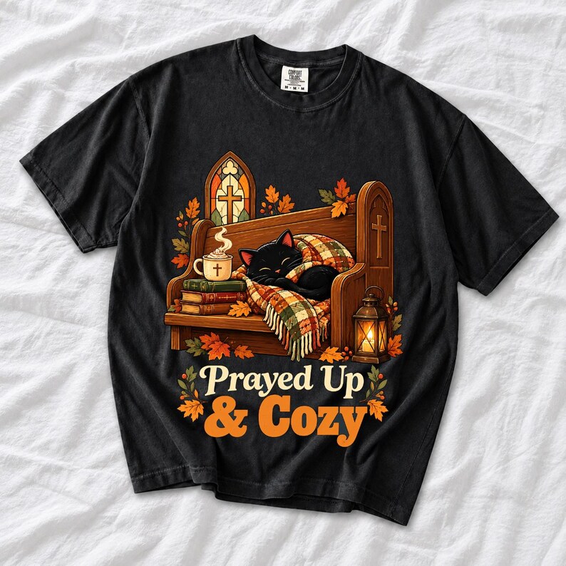 Black cat curled on a church pew with blanket and cocoa among autumn leaves, text "Prayed Up & Cozy", retro illustration