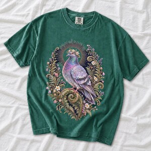 Painted pigeon wearing a daisy crown and glowing halo standing on a fern frond, whimsical cottagecore bird t-shirt art