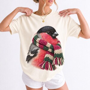 Colored-pencil bullfinch bird wrapped in a chunky striped knit scarf, cozy winter birdwatcher t-shirt art
