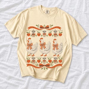 Three fluffy hens with gingham bows between apple and wheat borders, retro folk art fall t-shirt design