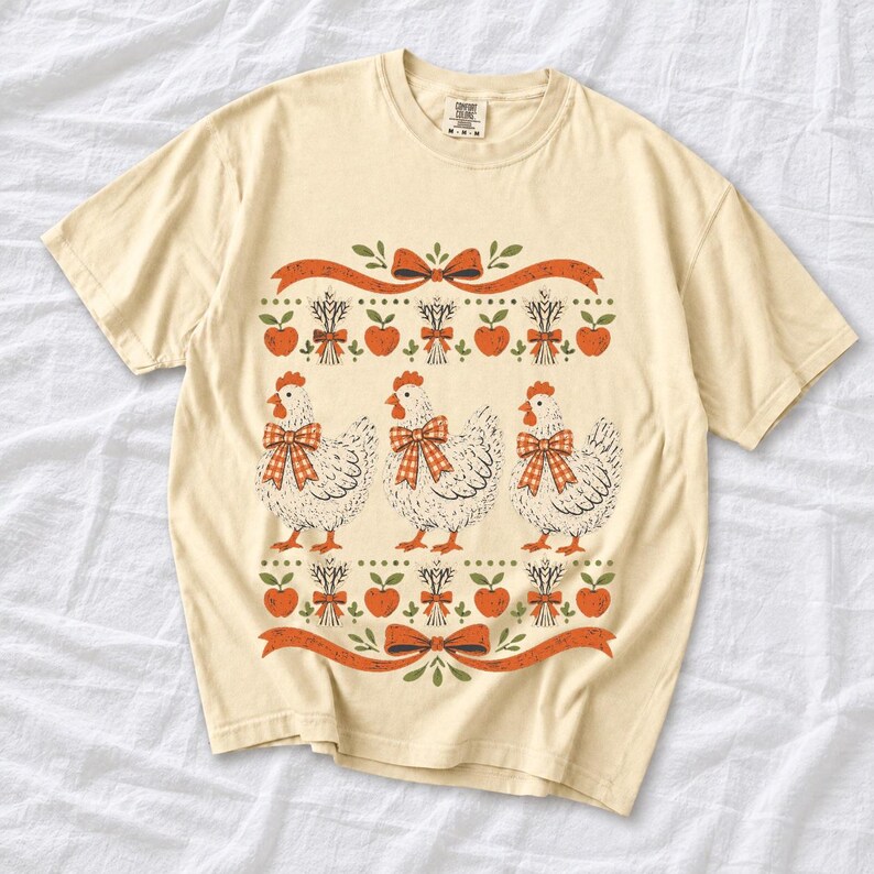 Three fluffy hens with gingham bows between apple and wheat borders, retro folk art fall t-shirt design