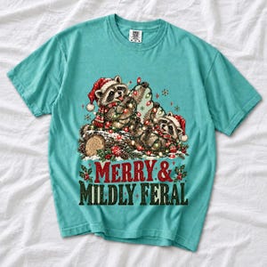 Two raccoons tangled in Christmas lights beside a log with the text Merry & Mildly Feral