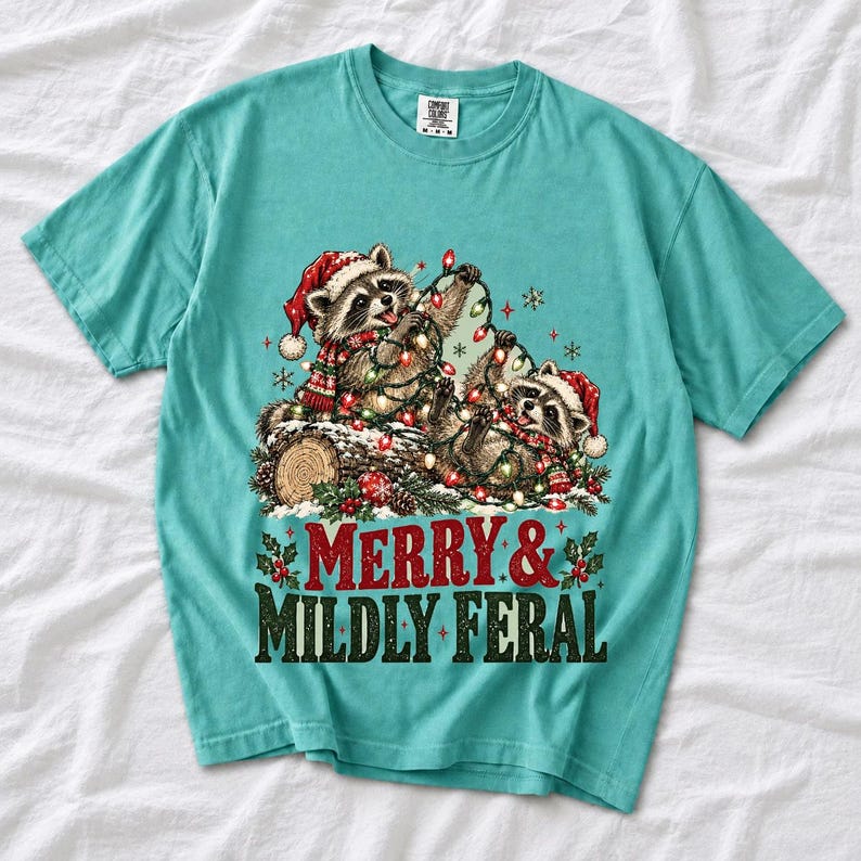 Two raccoons tangled in Christmas lights beside a log with the text Merry & Mildly Feral