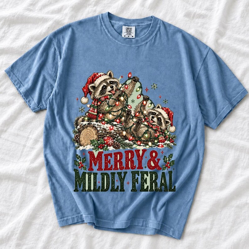 Two raccoons tangled in Christmas lights beside a log with the text Merry & Mildly Feral