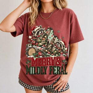Two raccoons tangled in Christmas lights beside a log with the text Merry & Mildly Feral