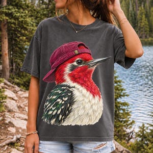 Colored-pencil red-headed woodpecker in side profile wearing a backwards corduroy cap, funny birder t-shirt graphic