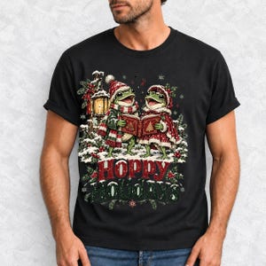 Two frogs singing carols in the snow with a lantern and songbook, text Hoppy Holidays