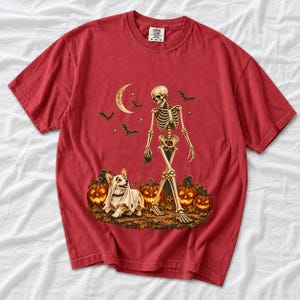 A skeleton walking a corgi in a ghost costume past carved pumpkins under a crescent moon