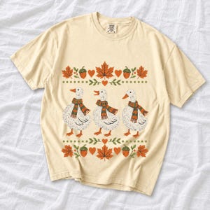 Three white ducks in striped scarves with acorn and maple leaf borders, retro screen print fall t-shirt art