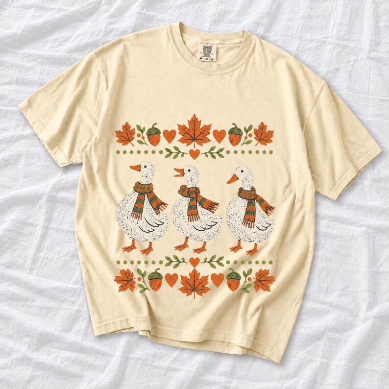 Three white ducks in striped scarves with acorn and maple leaf borders, retro screen print fall t-shirt art