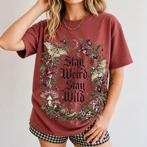 Victorian-style wreath of nightshade, luna moths and toadstools around the words "Stay Weird, Stay Wild"