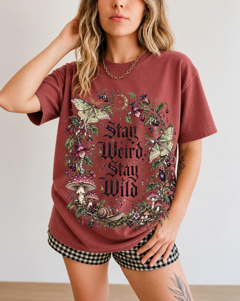 Victorian-style wreath of nightshade, luna moths and toadstools around the words "Stay Weird, Stay Wild"