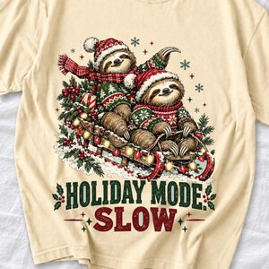 Two sloths in ugly sweaters riding a sled with lights and the text Holiday Mode: Slow