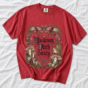 Blackletter text "Mushroom Witch Society" framed by fly agaric mushrooms, ferns and a toad on a mushroom cap