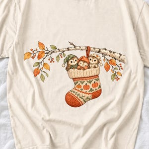 Three watercolor owlets in pajamas and nightcaps tucked into a knitted stocking on a birch branch, one asleep