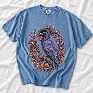 Raven holding a rowan berry inside an oval wreath of heather and catkins, painted cottagecore bird illustration