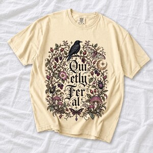 Raven on a wild rose branch with beetles and berries around blackletter text "Quietly Feral"
