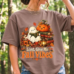 Smiling pumpkin with a halo beside a stack of books and a lantern, text "Lord, Give Me Fall Vibes", retro fall illustration