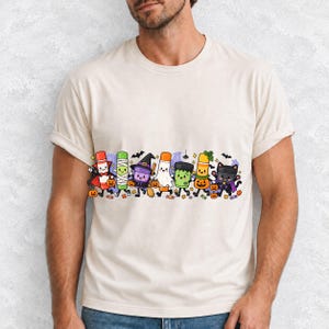 Seven glue sticks and paint pots with faces in Halloween costumes marching past pumpkins and cobwebs