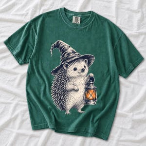 Etched pen illustration of a hedgehog in a witch hat holding a lantern, bone white with orange accent