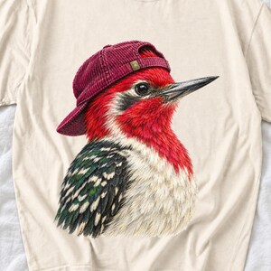 Colored-pencil red-headed woodpecker in side profile wearing a backwards corduroy cap, funny birder t-shirt graphic