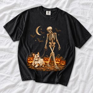 A skeleton walking a corgi in a ghost costume past carved pumpkins under a crescent moon