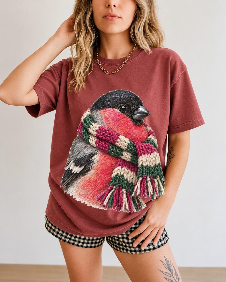 Colored-pencil bullfinch bird wrapped in a chunky striped knit scarf, cozy winter birdwatcher t-shirt art