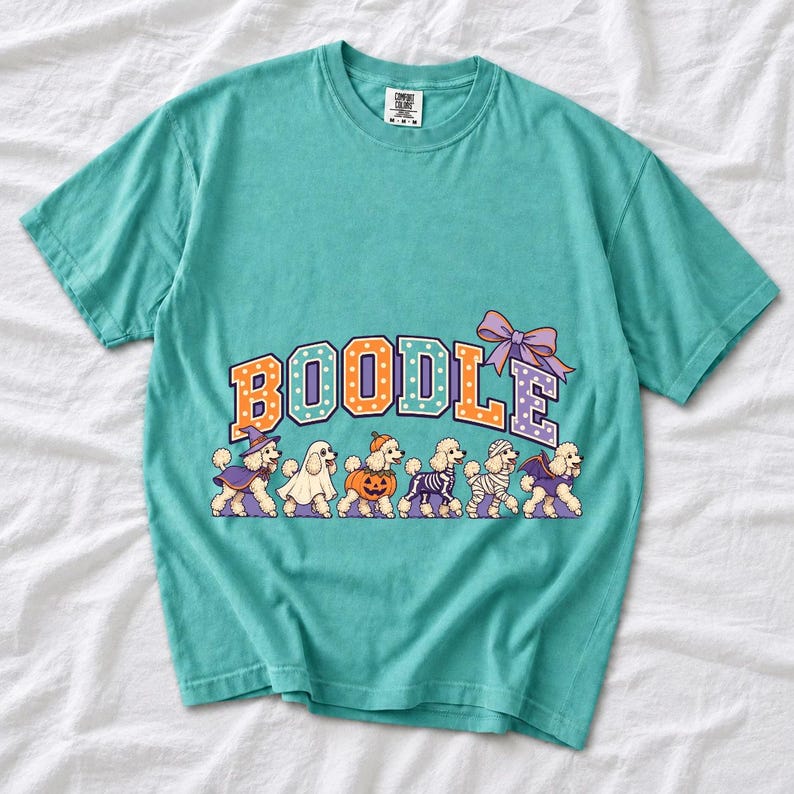 Six poodles in Halloween costumes walking under the arched word BOODLE, lavender and orange polka-dot varsity style