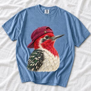 Colored-pencil red-headed woodpecker in side profile wearing a backwards corduroy cap, funny birder t-shirt graphic