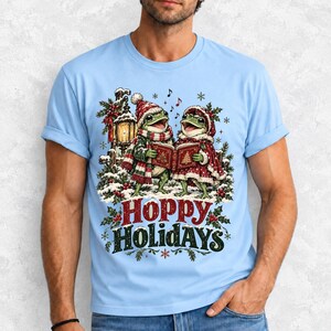 Two frogs singing carols in the snow with a lantern and songbook, text Hoppy Holidays