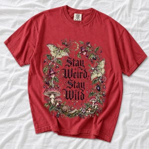 Victorian-style wreath of nightshade, luna moths and toadstools around the words "Stay Weird, Stay Wild"