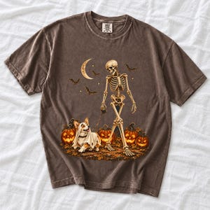 A skeleton walking a corgi in a ghost costume past carved pumpkins under a crescent moon
