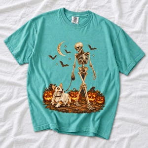 A skeleton walking a corgi in a ghost costume past carved pumpkins under a crescent moon