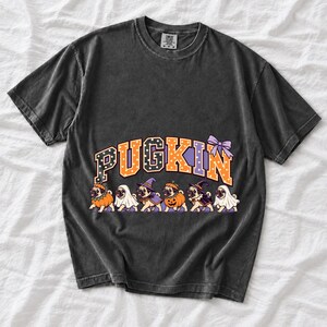 Six pugs in pumpkin, ghost and witch costumes under the arched word PUGKIN, lavender and orange polka-dot varsity style