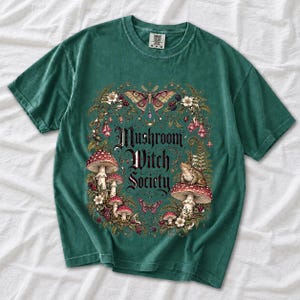 Blackletter text "Mushroom Witch Society" framed by fly agaric mushrooms, ferns and a toad on a mushroom cap