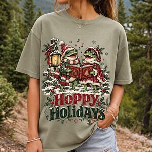 Two frogs singing carols in the snow with a lantern and songbook, text Hoppy Holidays