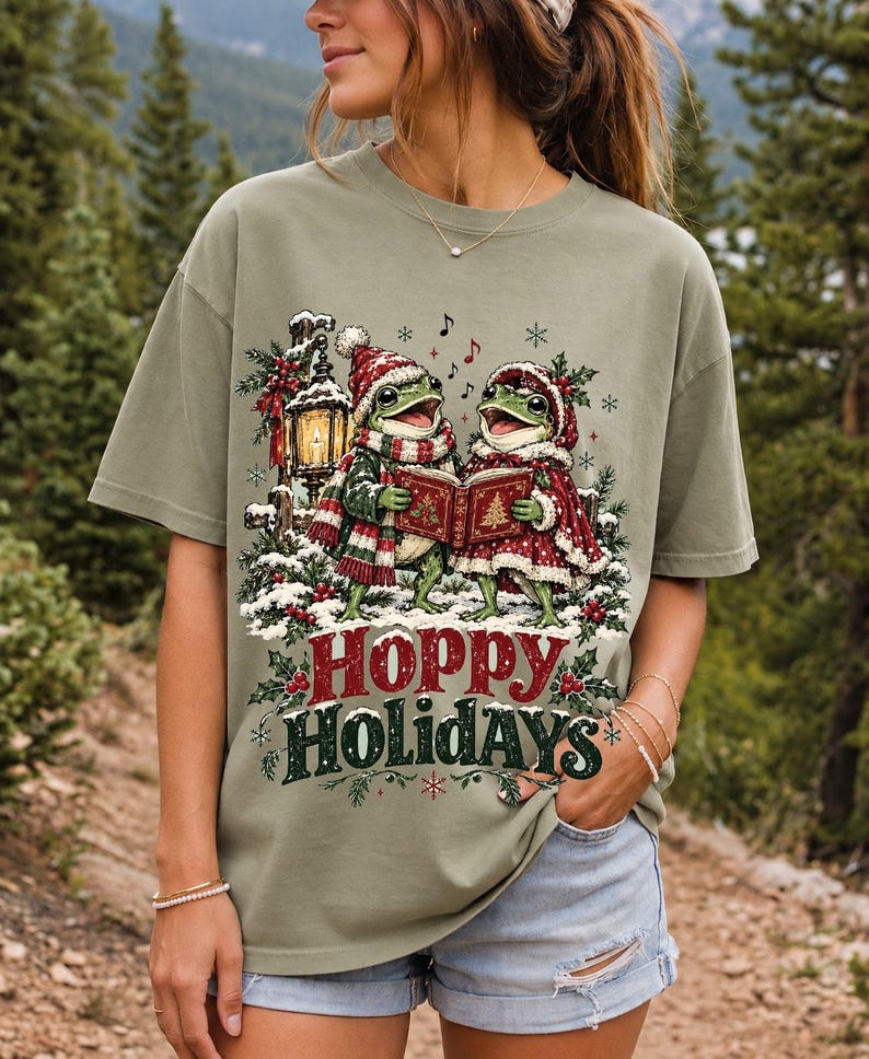 Two frogs singing carols in the snow with a lantern and songbook, text Hoppy Holidays