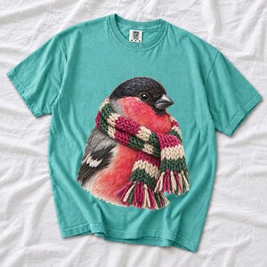 Colored-pencil bullfinch bird wrapped in a chunky striped knit scarf, cozy winter birdwatcher t-shirt art