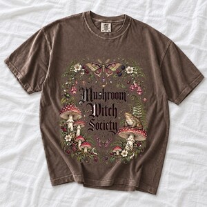 Blackletter text "Mushroom Witch Society" framed by fly agaric mushrooms, ferns and a toad on a mushroom cap
